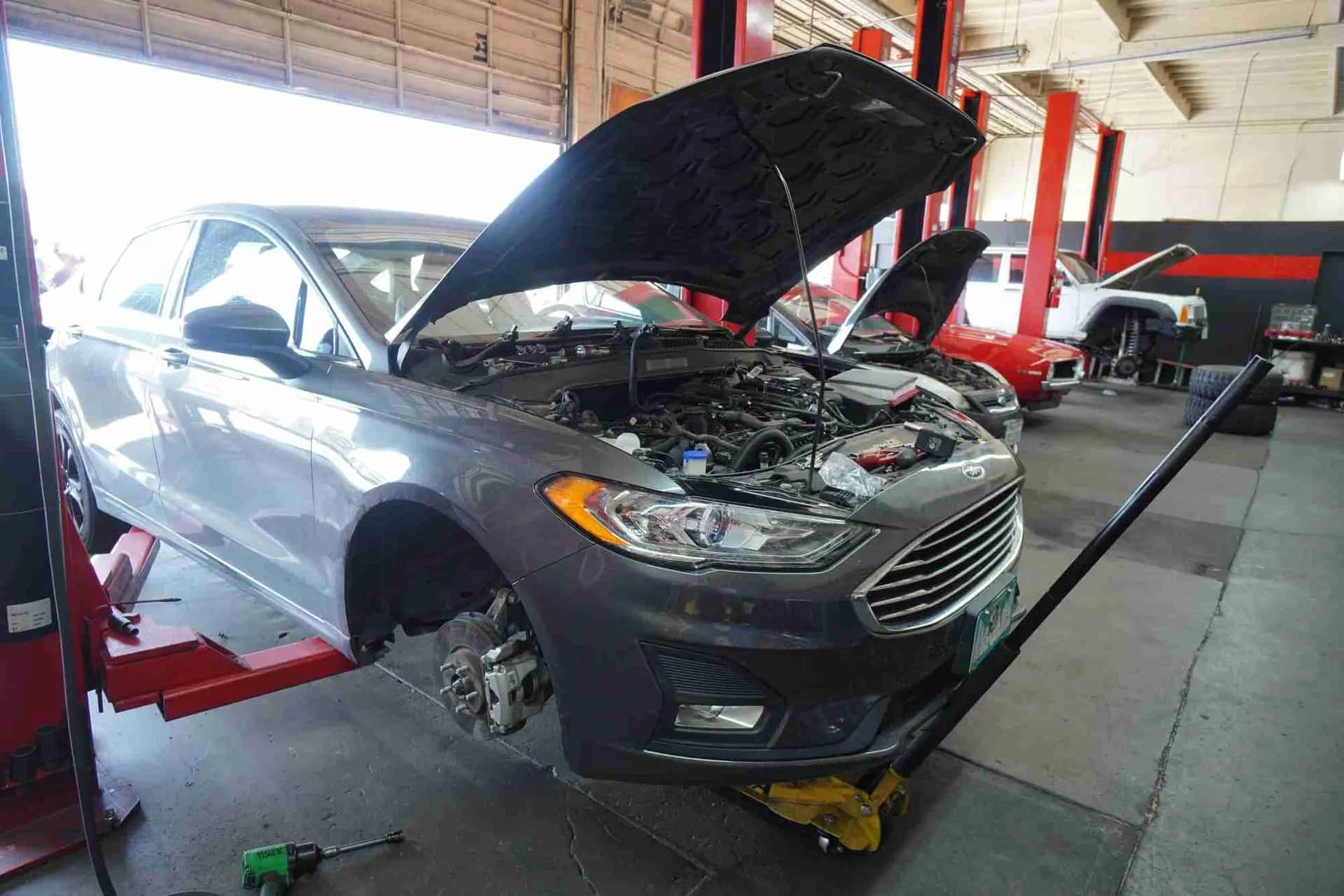 Car on a lift with the hood open and a front wheel removed for brake work