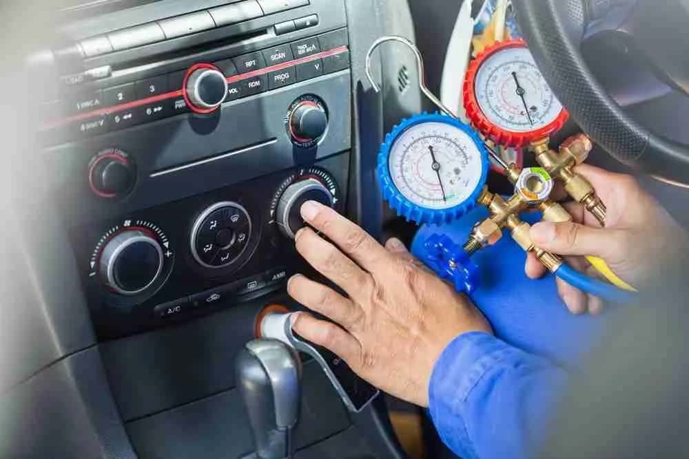 Technician adjusting car climate controls while reading AC gauges