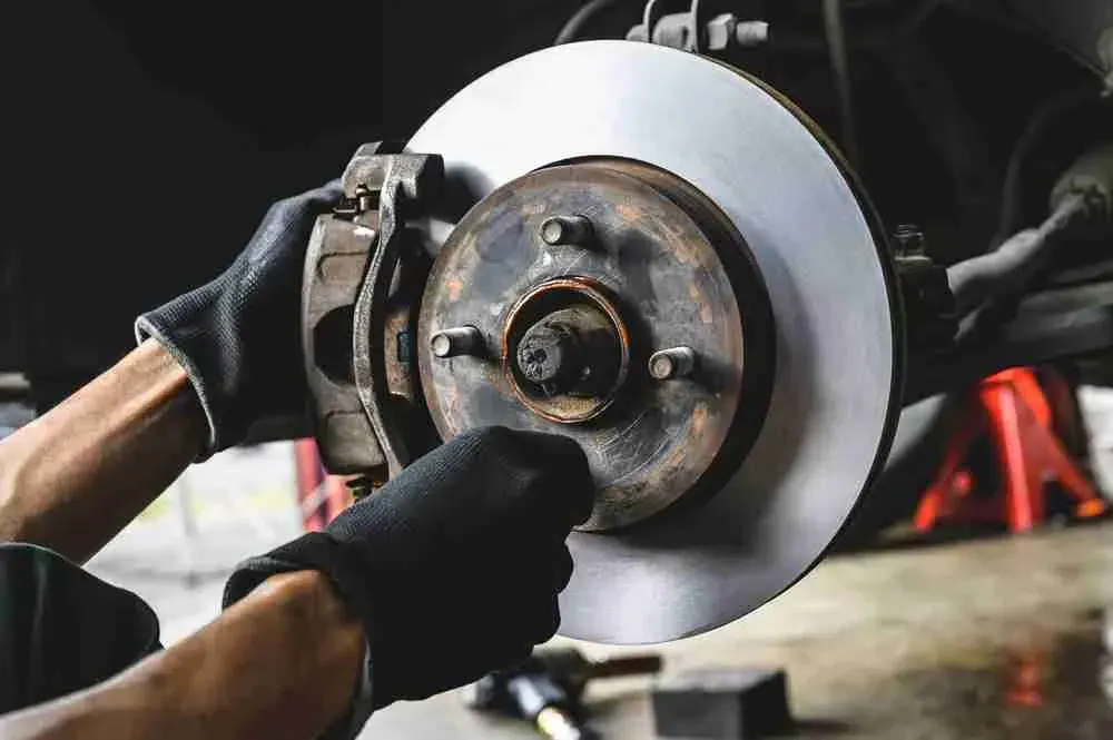 Gloved technician inspecting a brake rotor and caliper