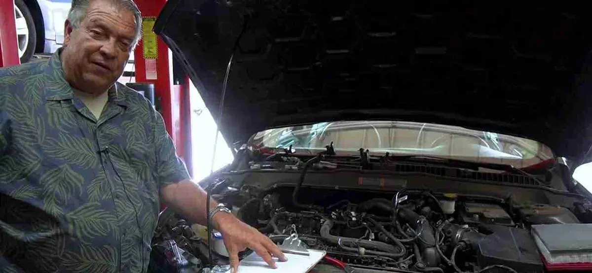 Shop team member explaining a repair beside an open engine bay