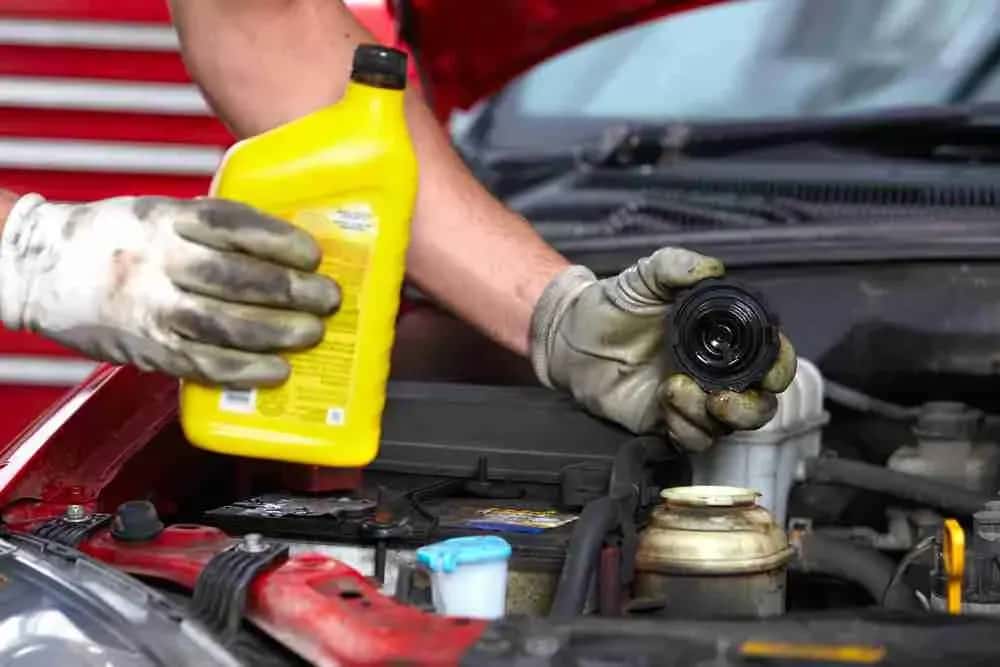 Gloved hands pouring fresh motor oil into an engine