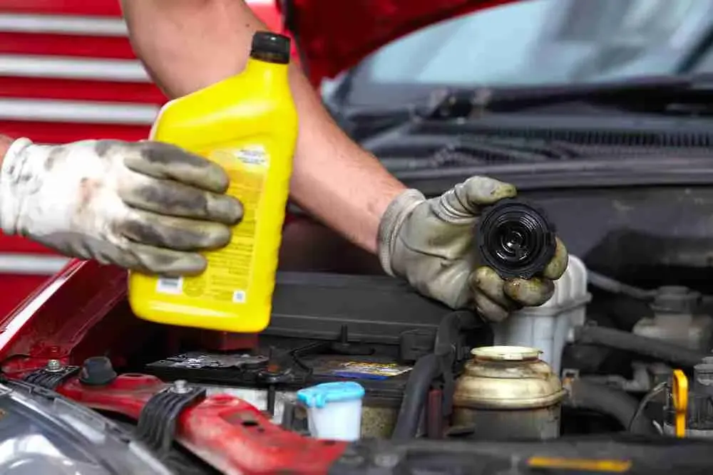 Gloved hands pouring fresh motor oil into an engine